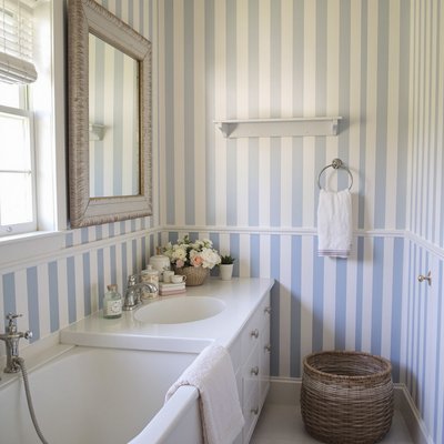 Gemütliches, im Landhausstil gehaltenes Badezimmer mit blau-weiß gestreifter Tapete.