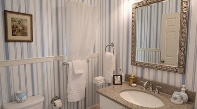 Gemütliches, im Landhausstil gehaltenes Badezimmer mit blau-weiß gestreifter Tapete.