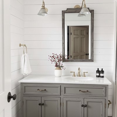 Bauernhaus-Badezimmer mit weißen Shiplap-Wänden, vintage Messingarmaturen und einem antiken Waschtisch