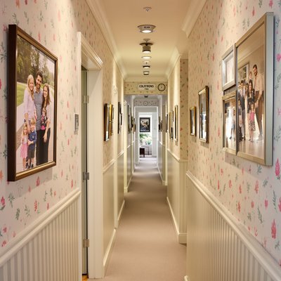 Schmaler, länglicher Korridor mit Pastelltapete und aufgehängten Familienfotos.