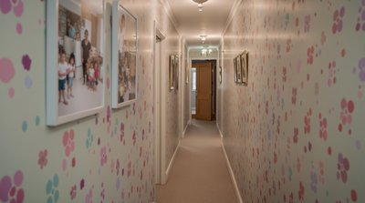 Schmaler, länglicher Korridor mit Pastelltapete und aufgehängten Familienfotos.