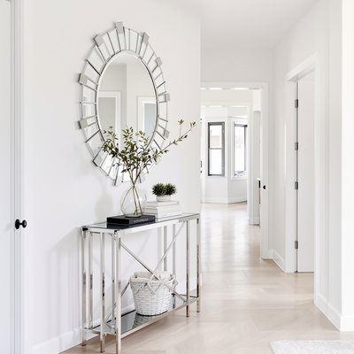 Zeitgenössischer heller Korridor mit geometrischen Spiegelakzenten und schlanker, metallener Konsolentisch