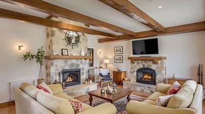 Rustikales Wohnzimmer mit Holzbalken, Steinkamin und gemütlichen Sofas.